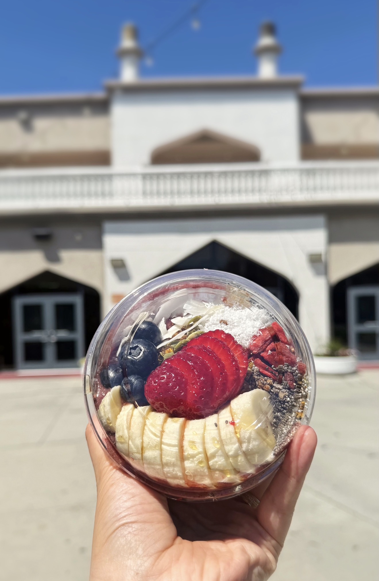 Açaí bowl held up with bananas, strawberries, blueberries, coconut, and chia seeds
